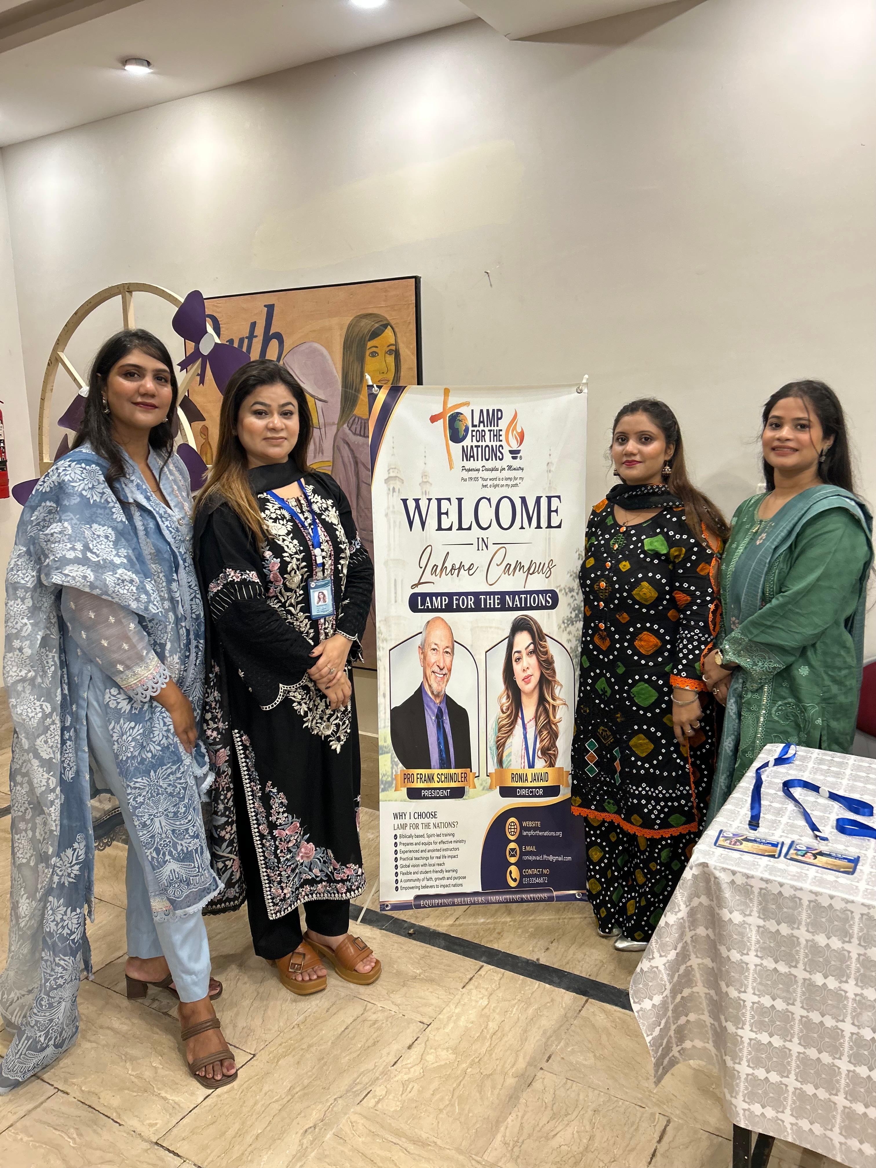 Four women standing beside the Lahore Campus welcome banner